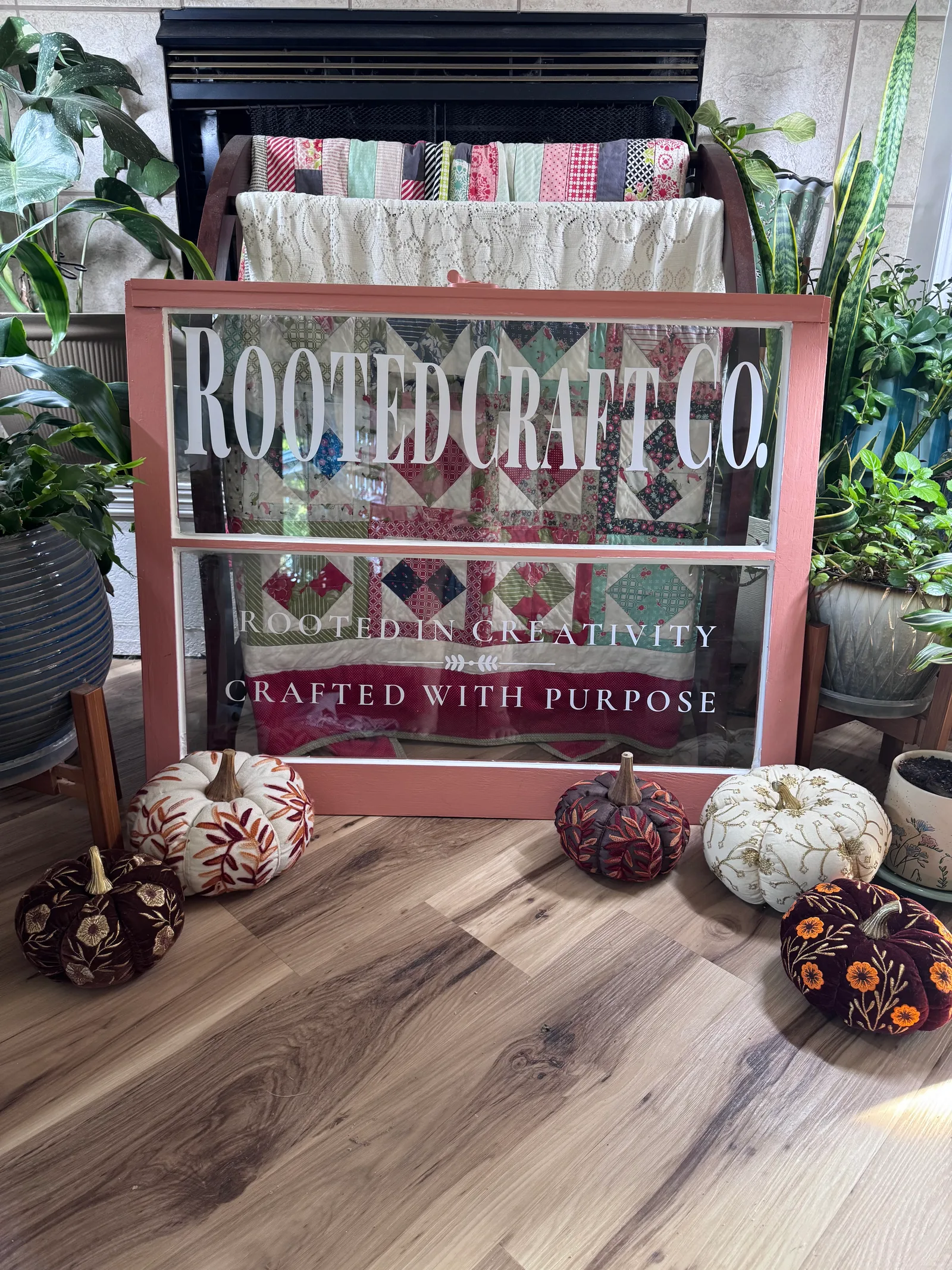 Pink Rooted Craft Co window sign surrounded by houseplants and embroidered pumpkins